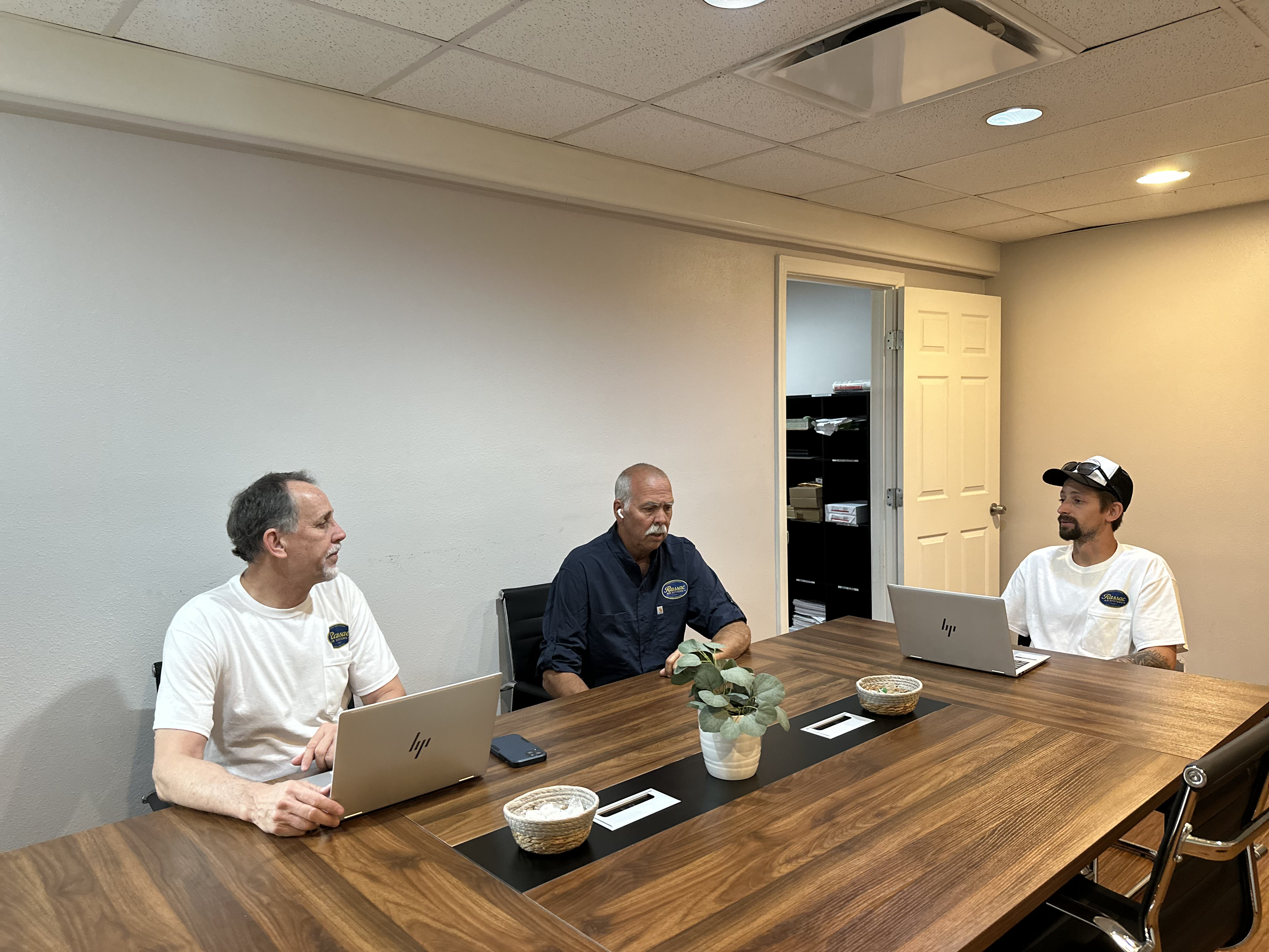 Meeting of three people in a workroom, two with laptops on the side, discussing professional topics in an office environment.